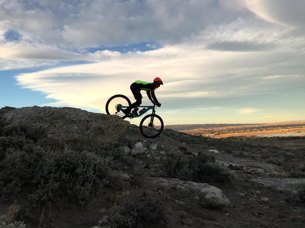 A mountain biker cresting a rocky ridge against a wide evening sky
